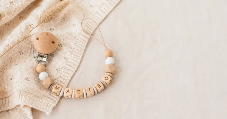 Finished handmade wooden dummy chain with letter beads and wooden clip on a cream-coloured knit baby cloth. A calming composition with plenty of negative space on the right for text overlay. Top-down view.